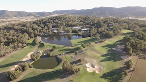 Luchtbeeld van een golfbaan met meerdere bunkers, een vijver en bebost gebied eromheen.