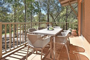 An outdoor patio with a table and chairs, a bottle of wine, and a glass.