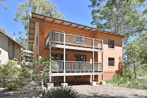 A two-story building with a balcony, surrounded by trees and vegetation.