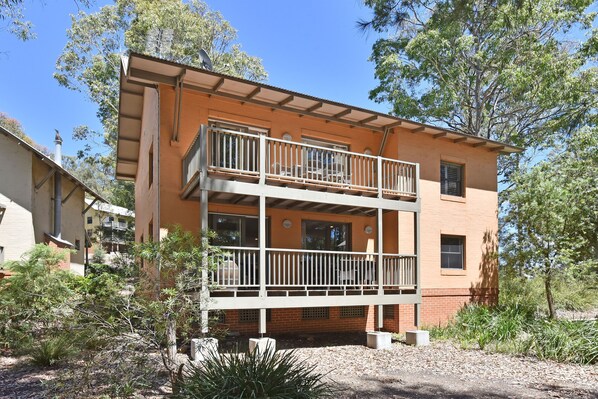 A two-story building with a balcony, surrounded by trees and vegetation.