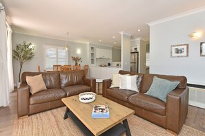 A modern living room with two brown leather sofas, a wooden coffee table, and a dining area with wooden chairs.
