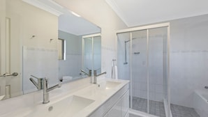 Une salle de bain moderne avec deux lavabos, un grand miroir et une douche à parois de verre.