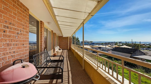 Un balcon avec un barbecue, des chaises et une vue sur la ville.