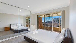 Une chambre dotée d’un grand miroir, d’un lit, d’une table de chevet et offrant une vue sur la ville depuis un balcon.