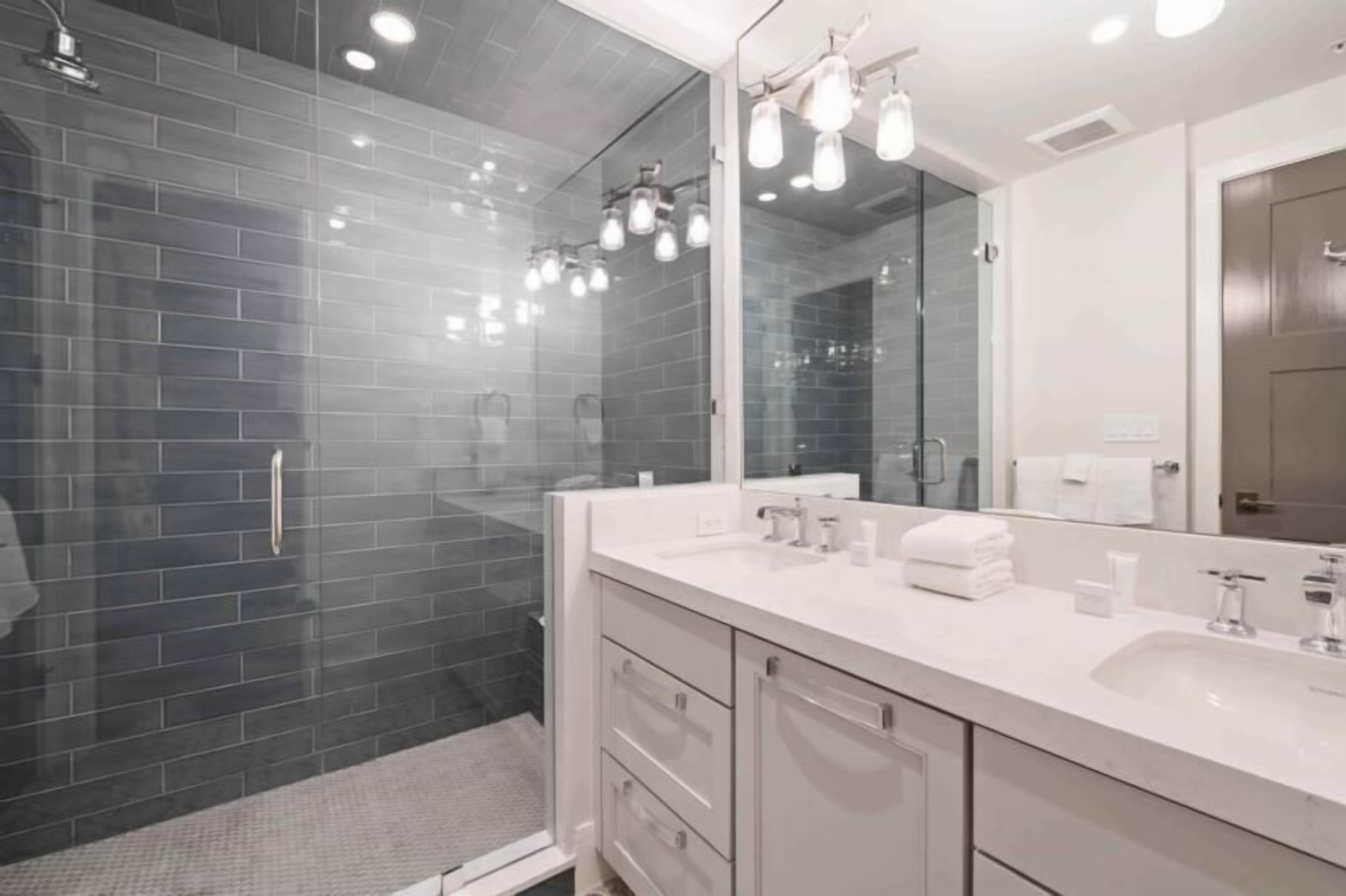 A modern bathroom with a glass shower enclosure, a white vanity with a large mirror, and a dark tiled shower wall.