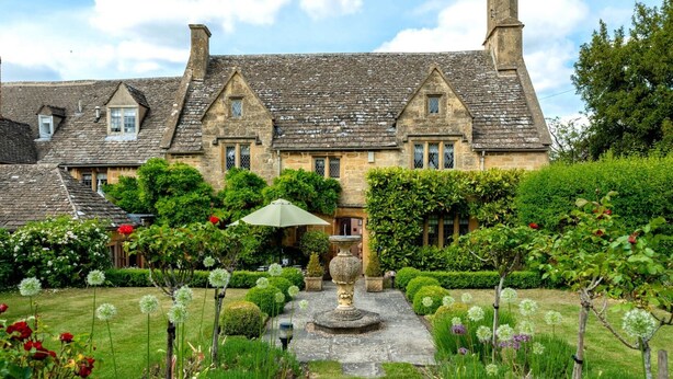 Un bâtiment traditionnel en pierre, doté d’une façade symétrique, d’un jardin central avec une fontaine et de haies bien entretenues.