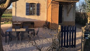 Un edificio rústico de piedra con tejado de tejas, una puerta de madera y un banco en el exterior.