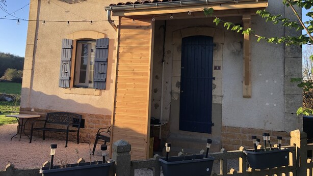 Un edificio rústico con puerta de madera, una ventana con persianas y un banco en el exterior.