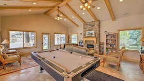 Un vaste salon doté d’une table de billard, de sièges confortables, d’une cheminée et de grandes fenêtres offrant une vue sur l’extérieur.