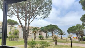 A view from a window overlooking a landscaped garden with various trees and a building in the background. - Spacious 2-Room Apartment with Pool & Sports Facilities, Sleeps 4 – Le Barcarès (Le Barcarès)