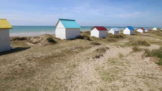 A row of beach huts with white walls and colorful roofs, situated on a sandy beach with dunes in the background. - 3-bedroom house, near beach, pets allowed, parking (Gouville-sur-Mer)
