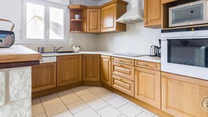 A modern kitchen with wooden cabinets, a built-in microwave, and a stove. - 3-bedroom house, near beach, pets allowed, parking (Gouville-sur-Mer)
