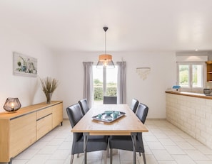 A modern kitchen with a wooden dining table, black chairs, and a pendant light. - 3-bedroom house, near beach, pets allowed, parking (Gouville-sur-Mer)