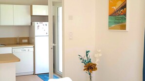 Una cocina compacta con armarios blancos, un refrigerador y una zona de comedor con mesa y sillas.