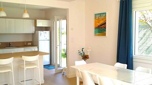 Una cocina moderna con armarios blancos, un refrigerador blanco y una encimera de madera. Hay una zona de comedor con una mesa y sillas blancas.