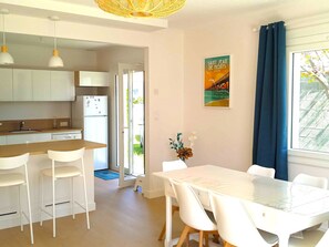 Eine moderne Küche mit weißen Schränken, einem weißen Kühlschrank und einer Holz Arbeitsplatte. Es gibt einen Essbereich mit einem weißen Tisch und Stühlen.