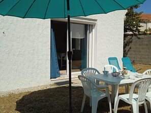 Une terrasse avec une table et des chaises blanches, un parasol turquoise et une porte-fenêtre coulissante.