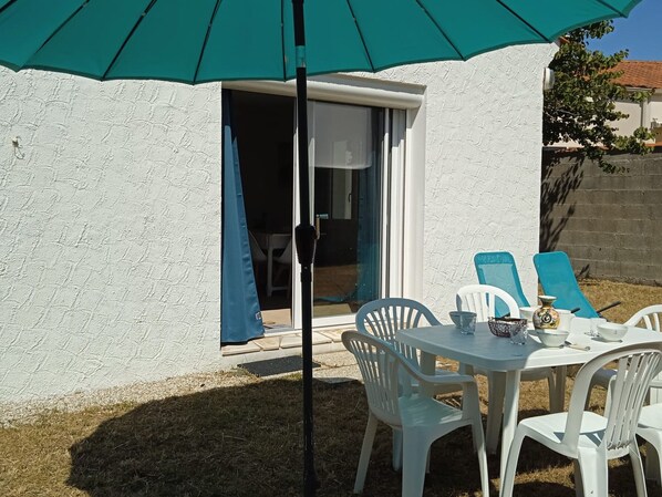 A patio with a white table and chairs, a teal umbrella, and a sliding glass door.