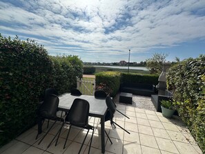 A patio with a table and chairs, surrounded by hedges and a view of a body of water.