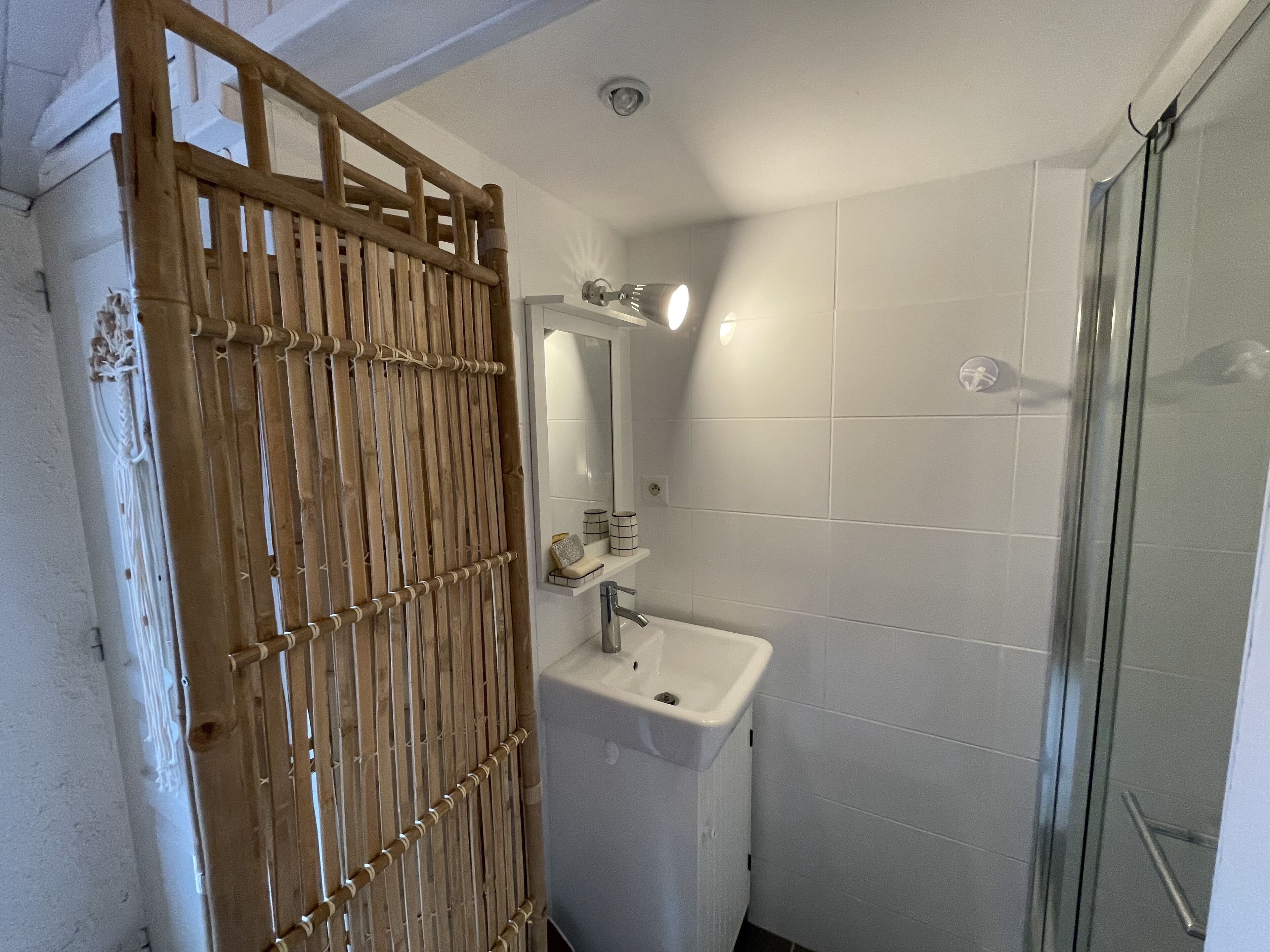 Een badkamer met een bamboe scheidingswand, een wastafel en een glazen douchecabine.