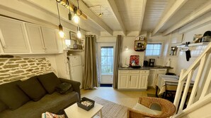 A cozy living room with a sofa, a small table, and a wicker chair. There is a kitchen area with cabinets and a dining table. - Ty Laouen, Peaceful fisherman's cottage, close to the beach, WIFI (Quiberon)