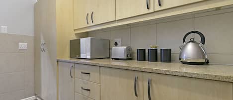 A modern kitchen with light wood cabinets, a granite countertop, a kettle, a toaster, and a microwave.