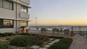 A hotel with a balcony overlooking the beach, potted plants, and outdoor seating. - Jacquelena Hof 9 (Cape Town)