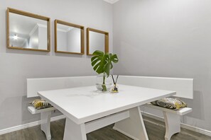 Uma mesa branca com bancos, uma planta em vaso e três espelhos com moldura de madeira na parede.
