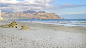 A beach with sand dunes, a sandy area with a sandcastle, and a mountain in the background. - Jacquelena Hof 9 (Cape Town)
