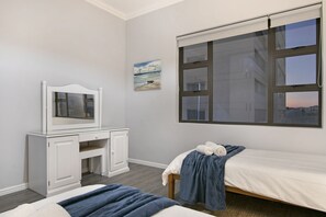 Quarto com cama, escrivaninha, cadeira, janela com persianas e um quadro na parede.