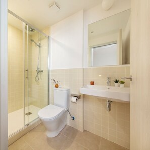 A bathroom with a glass-enclosed shower, a white toilet, a sink with a mirror, and a small plant on the sink. - Som Nit Port Vell (Barcelona)