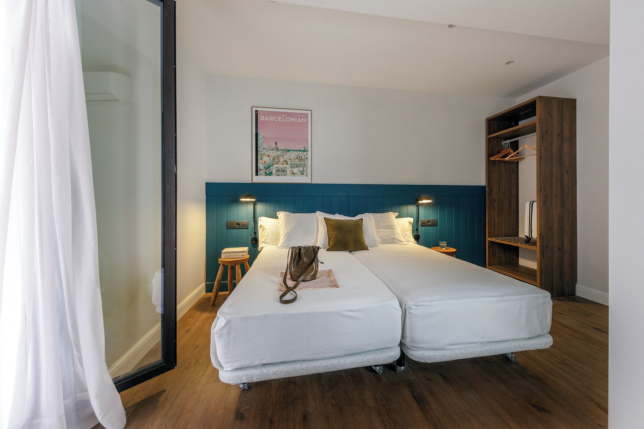 A double bed with a white duvet, a wooden headboard, and a poster of Barcelona on the wall.