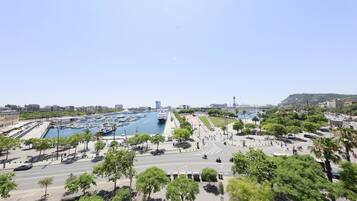 Un puerto deportivo con barcos amarrados, rodeado por un parque con árboles y un paseo marítimo.