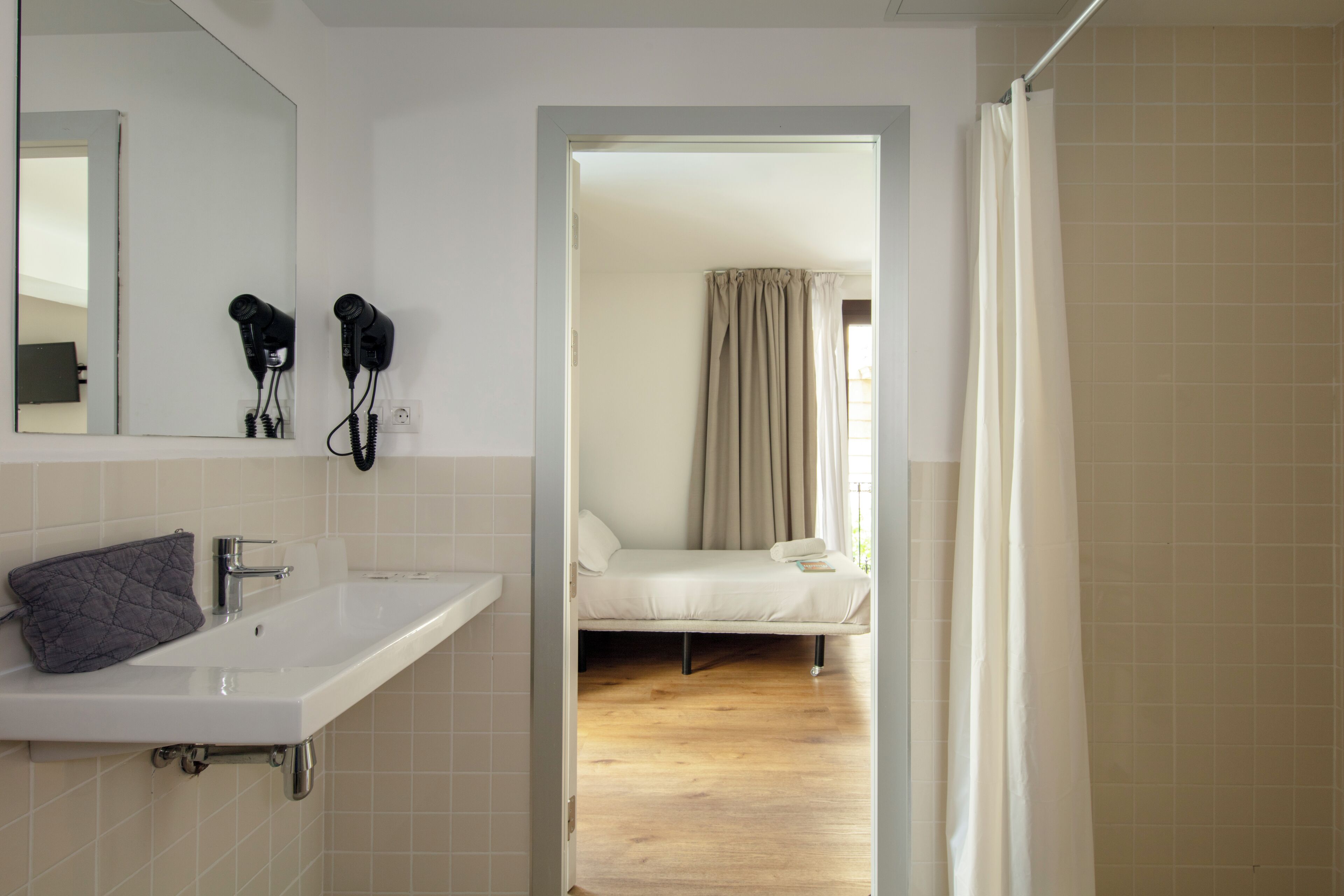 A bathroom with a white sink, a mirror, and two hair dryers mounted on the wall.