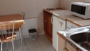 A compact kitchen with a wooden table, chairs, a microwave, a refrigerator, and a sink. - 1 Bedroom Apartment in Carnoux-en-Provence (Carnoux-en-Provence)