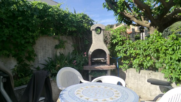 A patio with a stone-built outdoor oven, white plastic chairs, and a table with a patterned tablecloth. - 1 Bedroom Apartment in Carnoux-en-Provence (Carnoux-en-Provence)