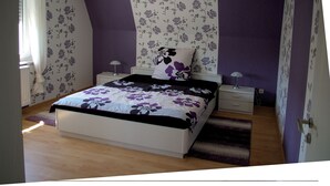 A bedroom with a bed, two bedside tables, a nightstand, a window with curtains, and a patterned wall. - Vacation home for max. 6 persons in Duhnen (Cuxhaven)