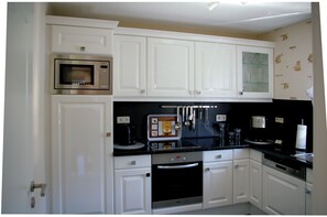 Compact kitchen with microwave, coffee maker, and oven, featuring a coffee-themed design.
