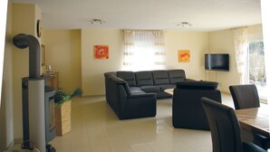 A living room with a sectional sofa, a dining table with chairs, a TV, and a fireplace. - Vacation home for max. 6 persons in Duhnen (Cuxhaven)