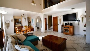 A spacious living room with a sofa, a coffee table, and a TV. There is a staircase leading to an upper level.