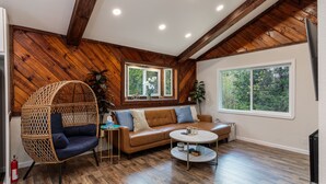 Una sala de estar acogedora con techo de madera, un sofá de cuero marrón, un sillón de mimbre y una mesa de centro redonda.