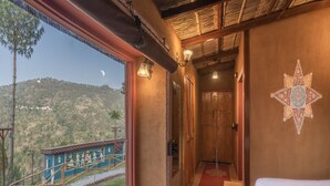 Una habitación con una cama, un ventanal con vistas a la montaña, una escalera y un detalle decorativo en la pared.