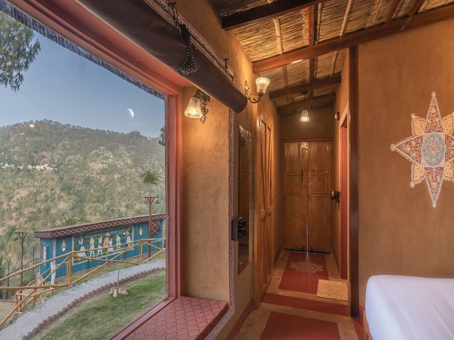 Una habitación con una cama, un ventanal con vistas a la montaña, una escalera y un detalle decorativo en la pared.