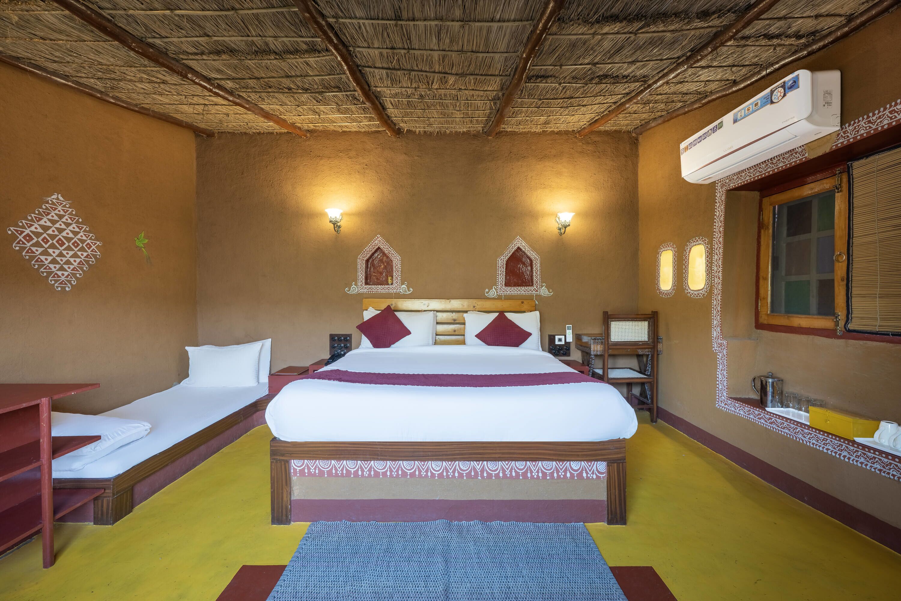 Habitación de hotel con cama, mesita de noche y un pequeño escritorio. Se ve una ventana con vistas al exterior.