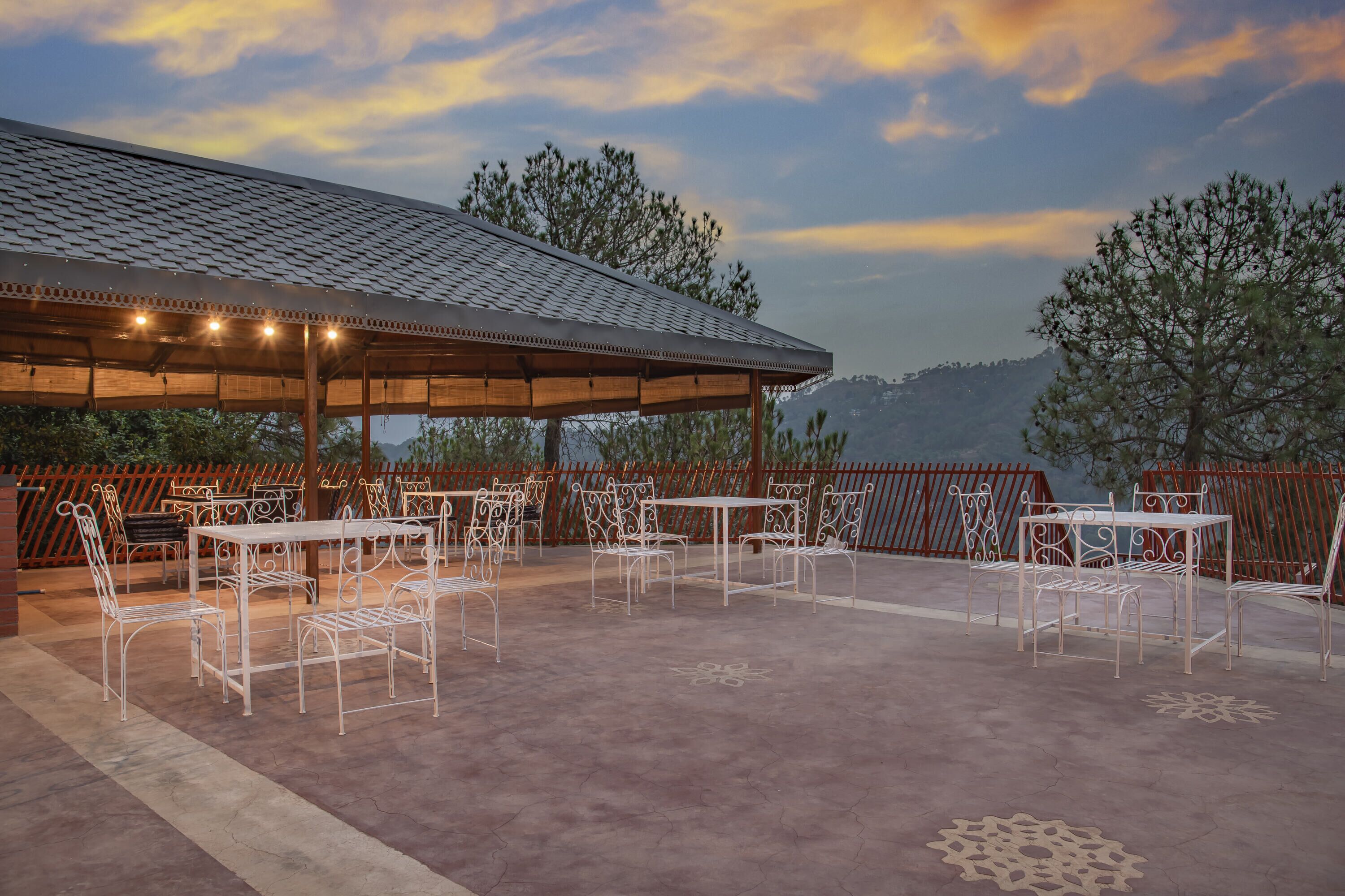 Un patio exterior con mesas y sillas, un área de estar techada y vistas a las montañas.