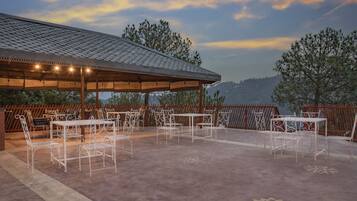 Un patio exterior con mesas y sillas, un área de estar techada y vistas a las montañas.