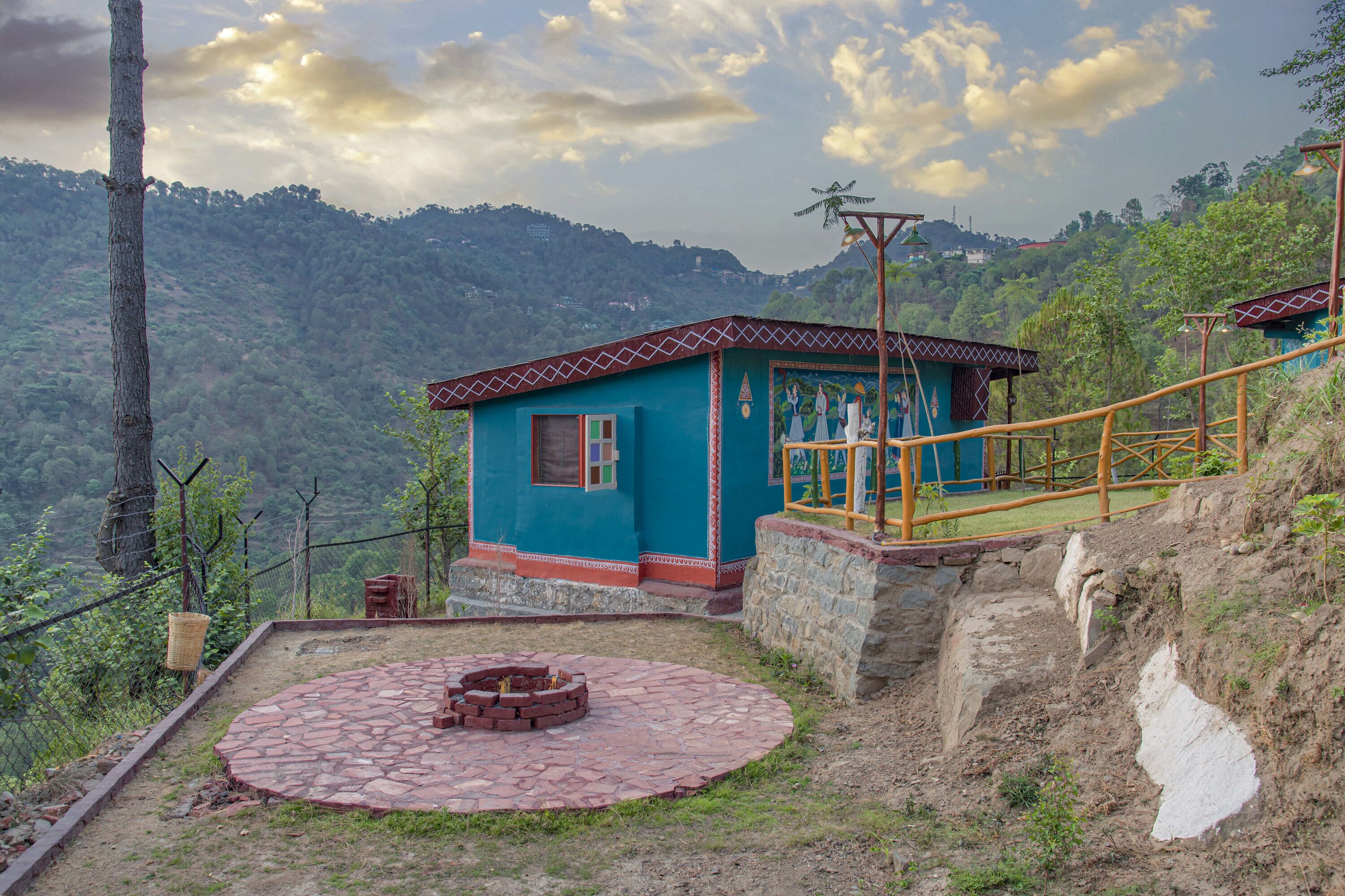 A blue house with a stone fire pit in the yard, surrounded by a stone wall and a wooden fence.