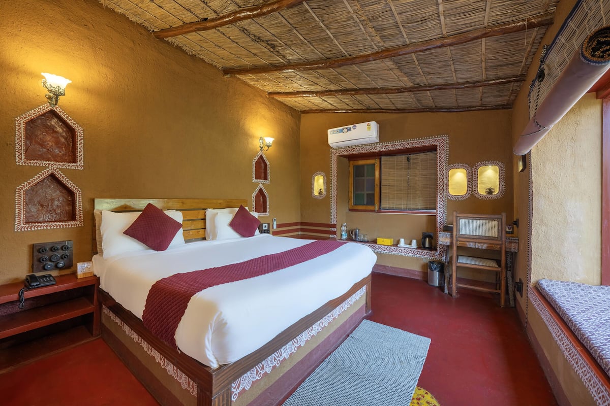 Habitación de hotel con una cama grande, cabecera de madera, mesita de noche con lámpara, un escritorio pequeño y una silla.