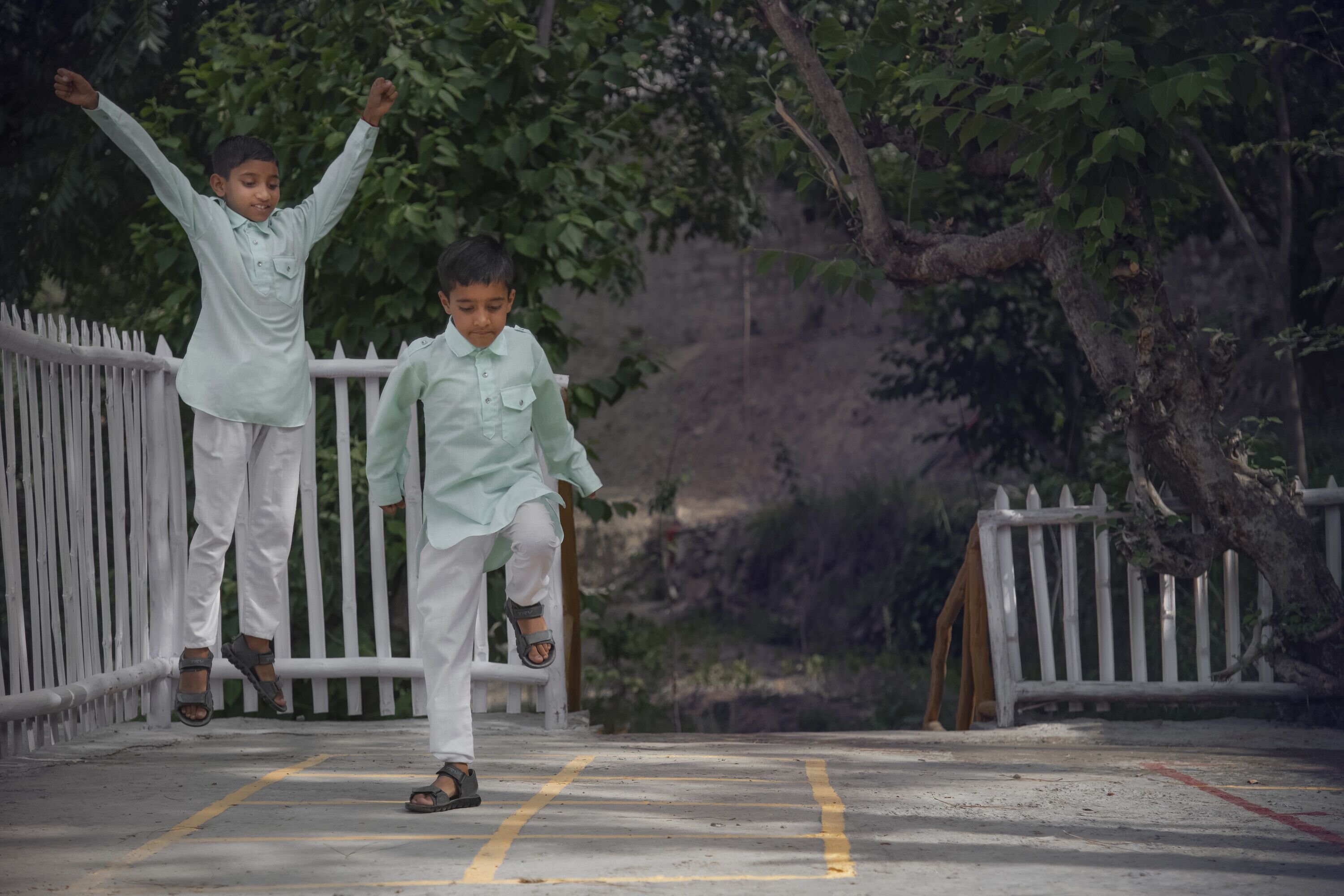Dos niños jugando sobre un puente de hormigón con barandillas blancas, rodeado de follaje.