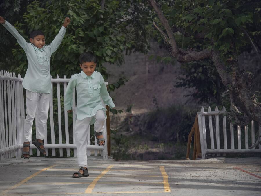 Two children playing on a concrete bridge with white railings, surrounded by greenery.